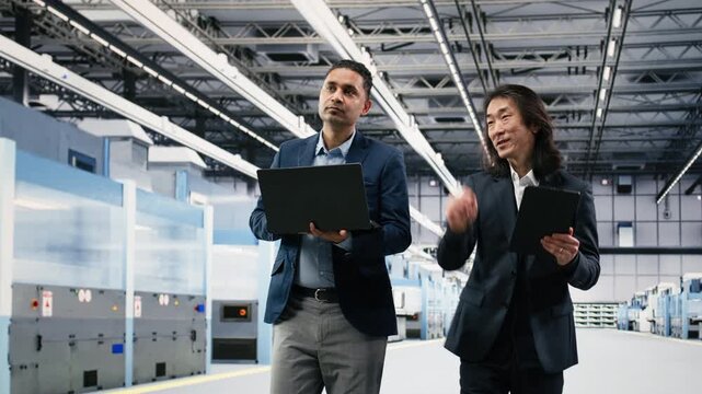 Multiracial management executives in microchip foundry brainstorming PCB components hardware fabrication steps. Senior manager and Indian man design semiconductors in manufacturing plant, camera B