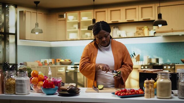 Cutting avocado, cooking video, recipe preparation on toast, black woman, food vlogger working at the counter. Influencer explaining culinary tutorial and meal prep, nutritious healthy choice.
