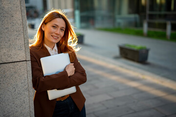 Professional woman carrying laptop smiling outdoors