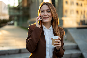Smiling businesswoman talking on smartphone holding coffee cup