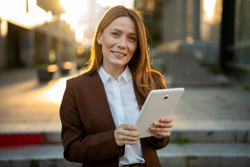 Professional businesswoman smiling while holding tablet in city street