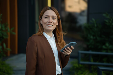 Businesswoman standing outdoors holding smartphone smiling