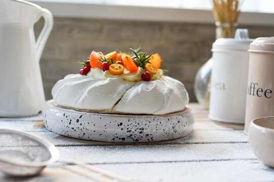 Gourmet pavlova cake topped with persimmon berries on speckled stand bright kitchen setting dessert.