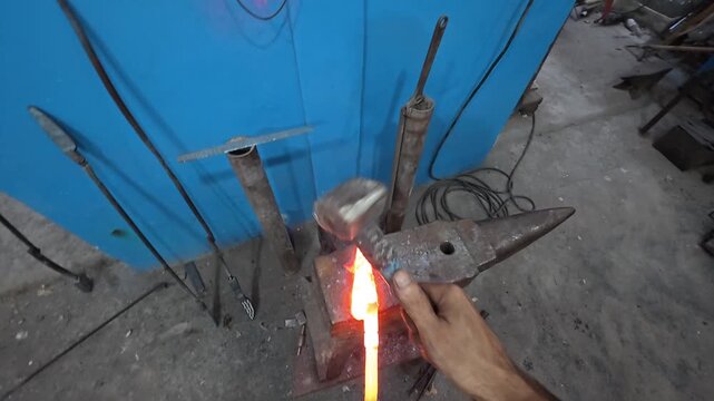 Artisan blacksmith forging a custom knife blade with a hammer and anvil in a traditional workshop. (POV)