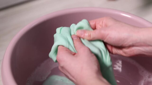 Woman washing stained kid's shirt in basinet at home, closeup