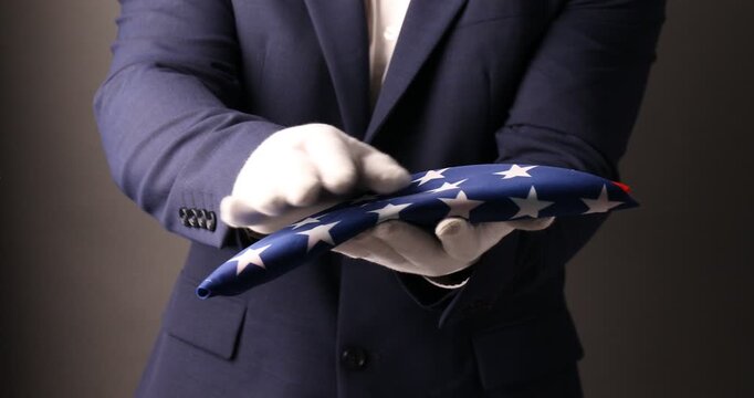 Official representative presenting folded US flag on grey background, closeup