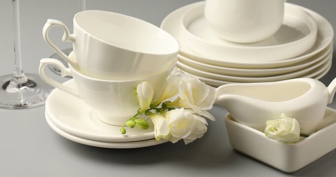 Woman putting beautiful flowers onto saucers and plates at grey table with other dishware, closeup
