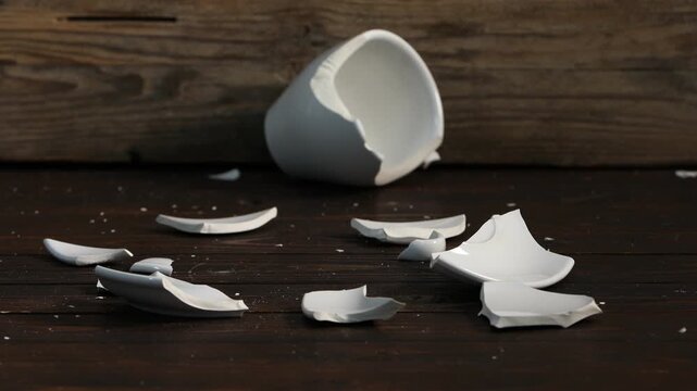Breaking white ceramic cup with hammer on wooden table, closeup