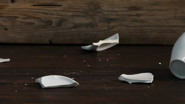 Cup falling and breaking saucer on wooden table, closeup