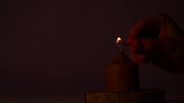 Woman hand lights a match the bees wax candle fire on wooden candlestick for mood, relaxation, meditation dark red background. Person lighting the decoration single candle flame