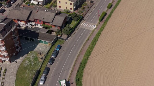 Urban Aerial View: An elevated view showcases a serene urban landscape, where structures align a winding road which borders a spacious farmland, offering a harmonious blend of urban and rural life. 