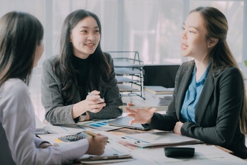 Fototapeta premium Three Asian businesswomen collaborate with business partners using laptop technology and graphical documents in a conference room of an office.