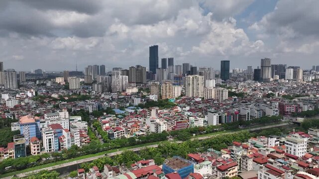 Aerial daytime view of Lang Street Hanoi with dense residential blocks, modern high rise skyline, and green corridor cutting through urban landscape under cloudy sky.