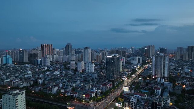 Blue hour aerial view of Tran Duy Hung and Lang Street Hanoi with dense residential blocks, modern high rises, and illuminated traffic corridor stretching across city.