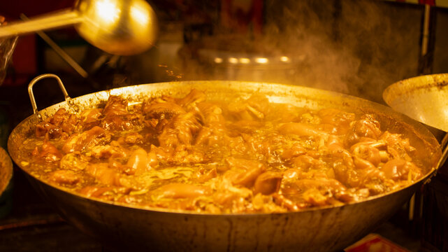 Hot meat stew cooking in large pan at night street market. Traditional dish with rich sauce and steam, authentic street food atmosphere.