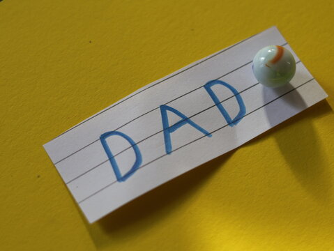 Una toma de cerca de la palabra padre en un papel blanco rodeado de canicas o metras en un fondo Amarillo para ser utilizado el d&iacute;a del padre
