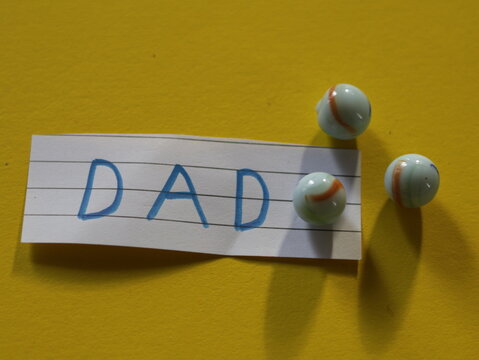 Una toma de cerca de la palabra padre en un papel blanco rodeado de canicas o metras en un fondo Amarillo para ser utilizado el d&iacute;a del padre