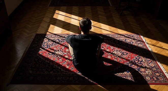 Man sitting on oriental rug in sunlit room with hard shadows on wooden parquet floor for meditation and peaceful contemplation in a quiet home