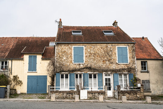 Front view of an old French residential house in a village, showing stone walls, blue shutters and tiled roof, illustrating traditional housing, rural property and vernacular architecture in France.