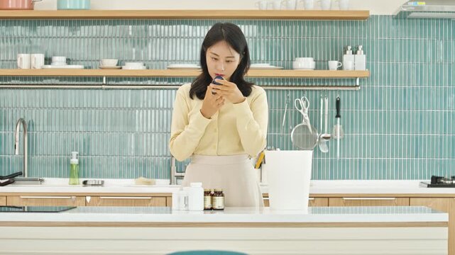 Young Asian woman carefully reading the label of a supplement bottle in a modern, clean kitchen, surrounded by other health products. Focus on wellness, daily routine, and informed choices.