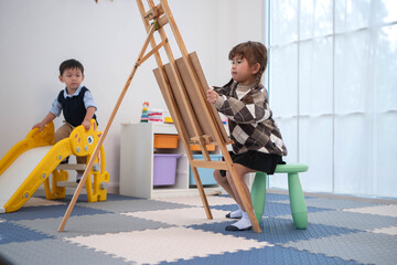 Naklejka premium Little girl drawing while a boy walks around, reflecting independent activities