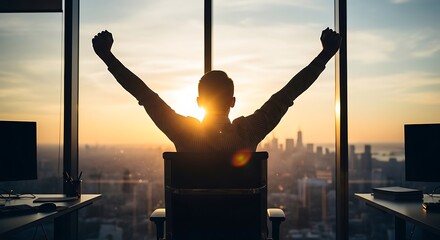 Fototapeta premium Silhouette of professional man sitting at desk with arms raised in celebration of business success overlooking a metropolis during golden sunset