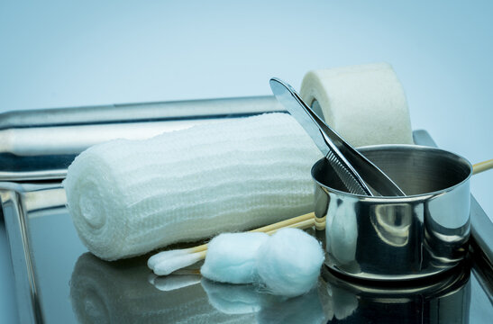 Wound care dressing set on stainless steel plate. Cotton ball with alcohol, cotton stick, surgical tape, forceps and conform bandage. Sterile medical supplies for treatment and infection prevention.