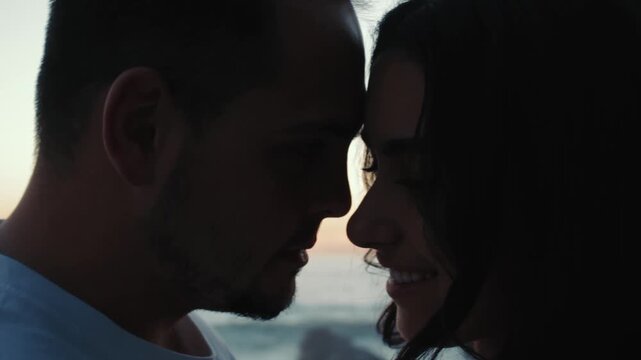 Romantic moment as man and woman gently touch foreheads with the sunset and sea in the background. Close up capturing love and connection