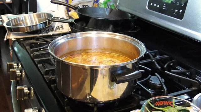 Zooming in on a simmering pot of soup on top of a stove.