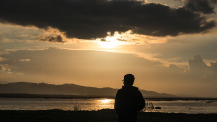 Fototapeta premium Man Silhouetted Against Golden Sunset Over Water