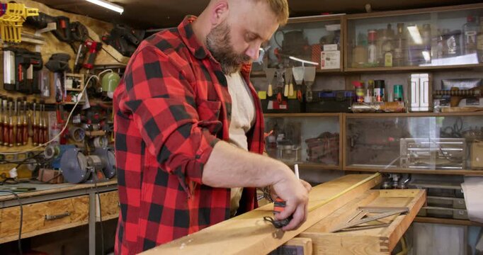 Measuring wood. Joinery workshop. Male carpenter with tape try square marking pencil lumber plank before cutting in industry interior.