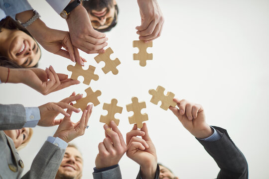 Jigsaw puzzles match, diverse colleagues holding wooden pieces, finding idea, searching business solution, solving problems together, employees in team building activity, support, close up bottom view