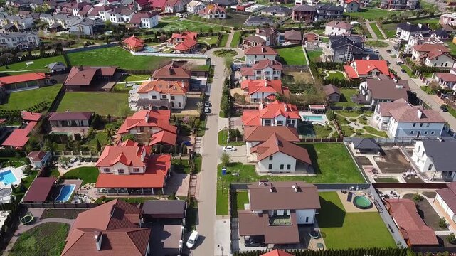 Aerial drone footage flying over a modern suburban neighborhood with private houses, green lawns, and streets on a sunny day in krasnodar