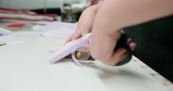 Garment making. Designer fabric. Woman hand working with scissors on tailoring studio table. Tailor creating clothes using curve cardboard draft.