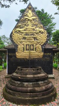 Golden Gunungan Wayang Monument with Javanese Script Inscription in a Lush Tropical Garden Park, Indonesia Traditional Culture Symbol and Heritage Architecture