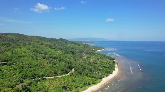Aerial drone footage nearby Tanjung Lesung beach park, in Pandeglang regency, Java island, Indonesia, with blue sea water, white sand beach, reef, forests and hills, in sunny weather, paradise road