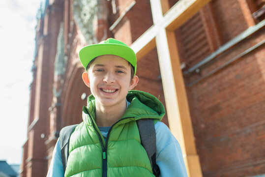  Smiling 13 year old teenage boy in green cap standing in front of a red brick Catholic church.