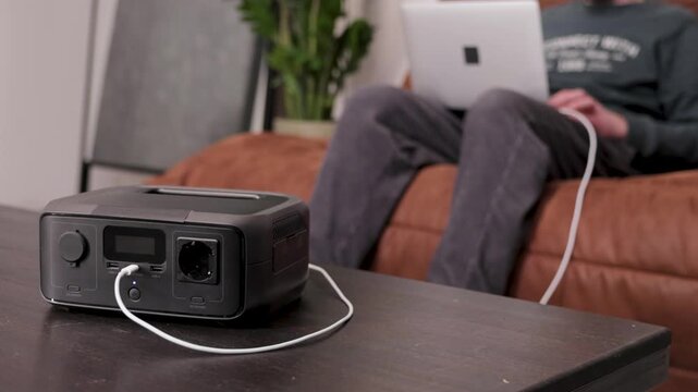 Portable power station on a table with a person working on a laptop in the background. Modern energy solution for home office or off-grid power.