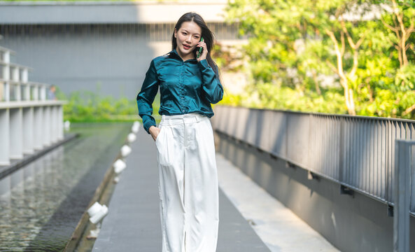 Happy young asian businesswoman talking on smartphone standing outdoor modern green office building, Confident freelancer, corporate lifestyle, mobile communication and business network concept