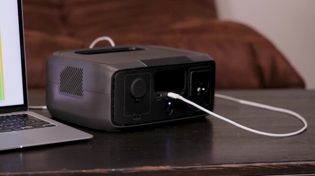 Portable power station on a table with a person working on a laptop in the background. Modern energy solution for home office or off-grid power.