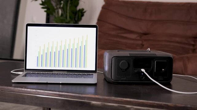 Portable power station on a table with a person working on a laptop in the background. Modern energy solution for home office or off-grid power.