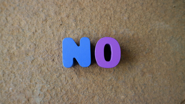 Colorful foam letters spelling no on textured beige surface, simple minimal flat lay with copy space, conveying refusal, rejection or negation concept.