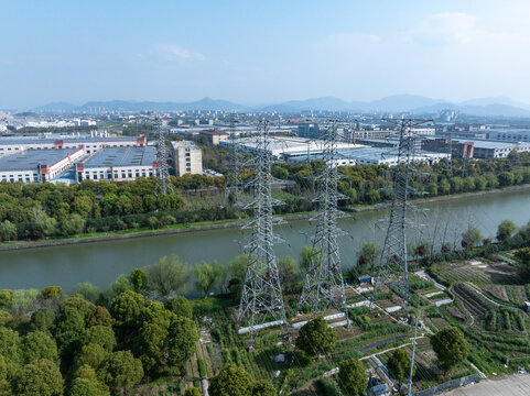 Aerial view of high-voltage transmission towers spanning a river near an industrial zone with factories and greenery