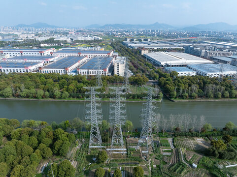 Industrial zone with high-voltage transmission towers alongside river and farmland landscape