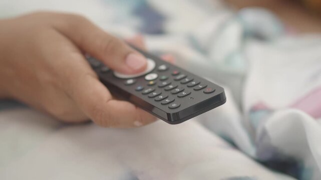 Person operating tv remote control lying in bed, changing channels in slow motion footage.