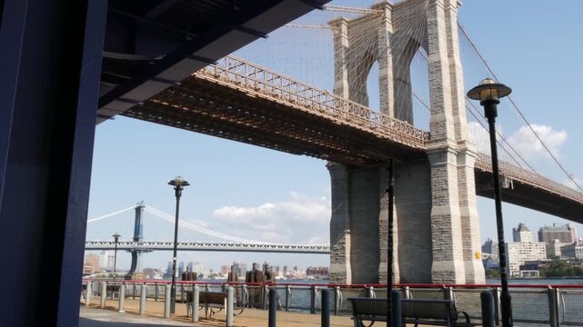Brooklyn Bridge and Manhattan Bridge from Downtown, New York City United States. Esplanade pier park in NYC USA. American architecture, famous tourist landmark. Waterfront urban promenade. Empty bench