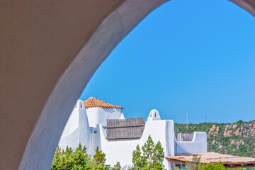 Whitewashed villa perched on rocky slopes, as seen through the arch, Porto Cervo, Sardinia, Italy