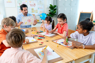 The teacher hold the picture that is the creation from kid in the classroom and give rating also ask for the idea and explaination from the owner. © narong