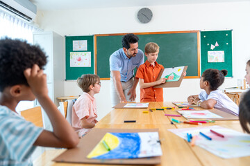 Wide shot of the teacher stand beside and try to make a boy with blond hair present his drawing or painting in front of the classroom and also ask the idea or the meaning of the picture. © narong