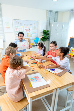 Vertical image of the teacher hold the picture that is the creation from kid in the classroom and give rating also ask for the idea and explaination from the owner.